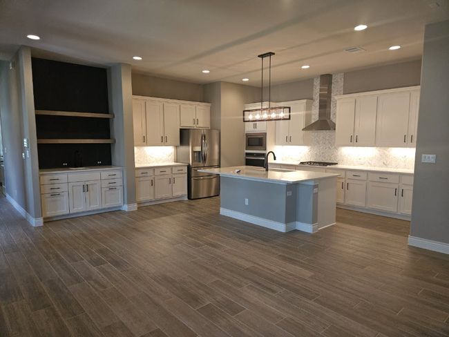 Kitchen with stainless steel appliances, wall chimney range hood, white cabinetry, decorative backsplash, and a center island with sink | Image 6