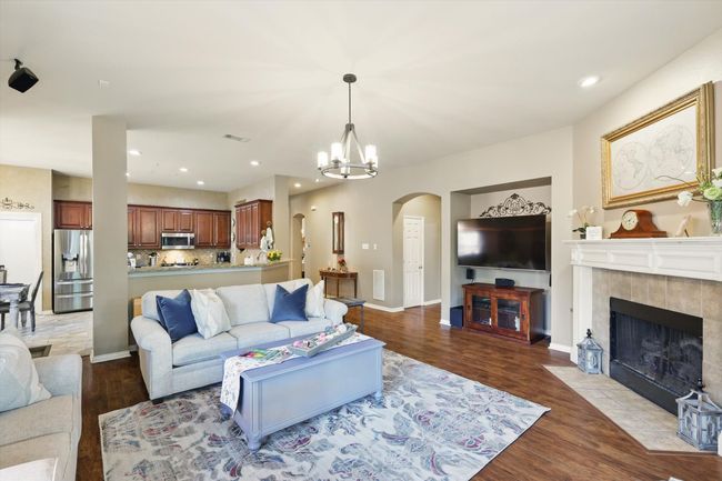 Living area featuring arched walkways, wood finished floors, a tiled fireplace, a chandelier, and baseboards | Image 8