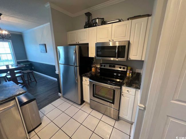 Kitchen with stainless steel appliances, ornamental molding, white cabinetry, light tile patterned flooring, and a chandelier | Image 4