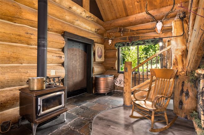 Living area with a wood stove, lofted ceiling, wooden ceiling, and rustic walls | Image 9