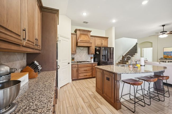Kitchen featuring custom exhaust hood, a sink, a breakfast bar, wood finish floors, and stainless steel appliances | Image 14