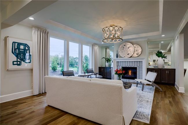 Living room featuring crown molding, an inviting chandelier, a raised ceiling, hardwood / wood-style flooring, and a tile fireplace | Image 4
