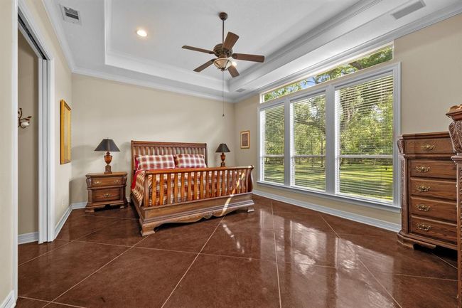 Tranquil owner’s retreat with soaring tray ceiling, ceiling fan, and a wall of picture windows plus high transom light—flooded with natural light and overlooking the lush backyard. | Image 23