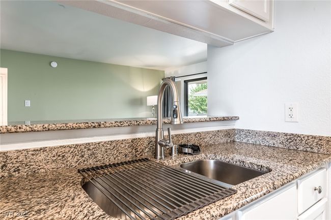 Kitchen view of white cabinets, a sink, and light stone counters | Image 17