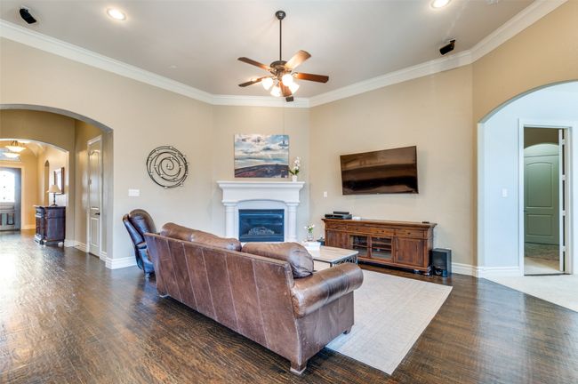 Living room with arched walkways, dark wood-style floors, ceiling fan, and a glass covered fireplace | Image 9