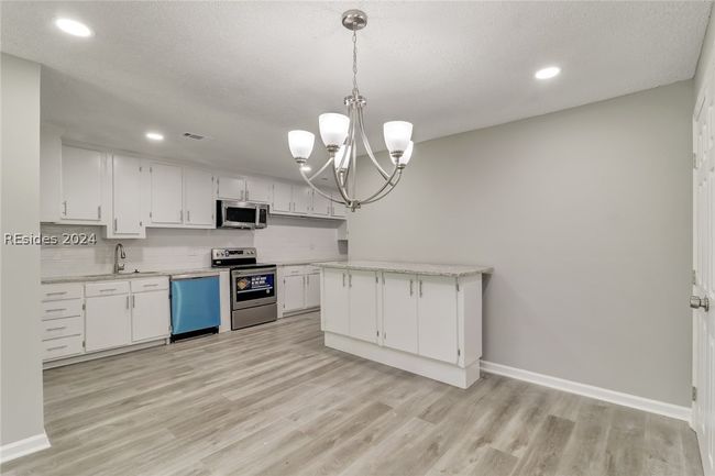 Kitchen featuring white cabinetry, stainless steel appliances, pendant lighting, sink, and light hardwood / wood-style flooring | Image 22