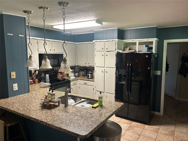 Kitchen featuring black appliances, a peninsula, light tile patterned floors, white cabinets, and a kitchen bar | Image 9