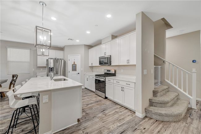 Kitchen with appliances with stainless steel finishes, a kitchen bar, light wood-style flooring, a kitchen island with sink, and white cabinets | Image 20