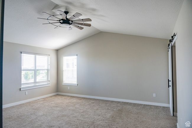 Spare room featuring vaulted ceiling, carpet flooring, a textured ceiling, a barn door, and ceiling fan | Image 14