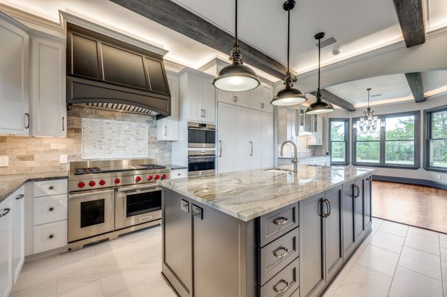 Kitchen with stainless steel appliances, decorative backsplash, an island with sink, light stone counters, and a chandelier | Image 4