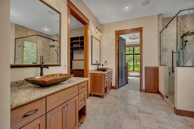 Modern glass-enclosed shower features a rainfall showerhead and mosaic tile accents. Parallel the shower sits a deep soaking tub, perfect for relaxing. | Image 49