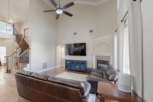Living room with stairway, a high ceiling, a ceiling fan, arched walkways, and a tiled fireplace | Image 4