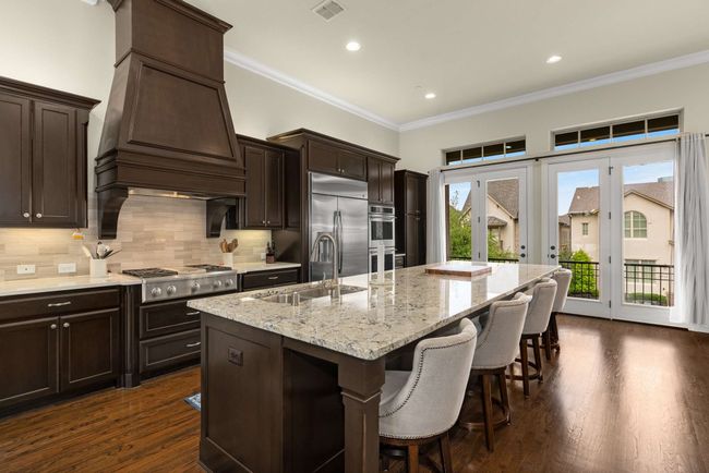 Kitchen with stainless steel appliances, custom exhaust hood, wood floors, and a kitchen island with sink. | Image 4