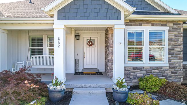Doorway to property featuring stone siding, board and batten siding, a porch, and roof with shingles | Image 43