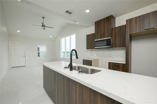 Kitchen with stainless steel microwave, a sink, ceiling fan, modern cabinets, and light marble finish floors | Image 9