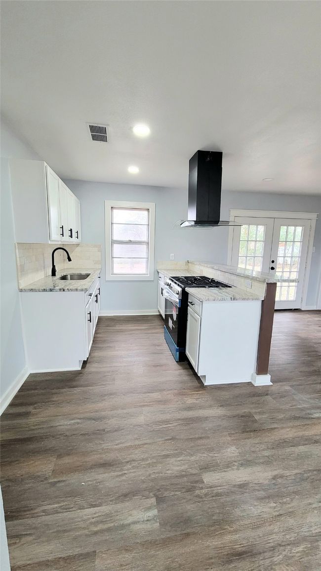 Kitchen featuring dark wood-style floors, range hood, visible vents, a sink, and gas range | Image 5