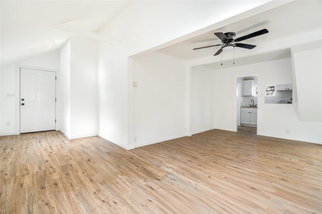 Unfurnished living room featuring a ceiling fan, baseboards, lofted ceiling, a sink, and light wood-type flooring | Image 4