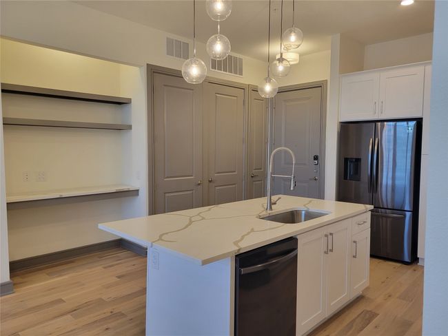 Kitchen with open shelves, visible vents, dishwashing machine, a sink, and stainless steel refrigerator with ice dispenser | Image 6