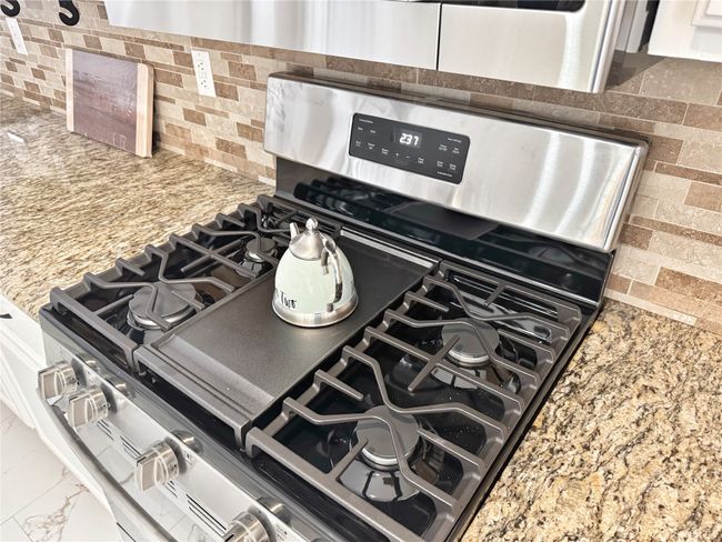 Kitchen view of stainless steel gas stove, backsplash, light stone counters, and white cabinetry | Image 11