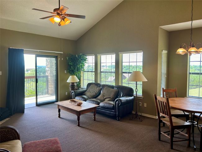 Carpeted living area featuring a chandelier, healthy amount of natural light, ceiling fan, and high vaulted ceiling | Image 9