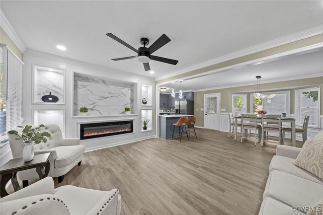 Living area featuring crown molding, light wood-style floors, a glass covered fireplace, a ceiling fan, and recessed lighting | Image 13