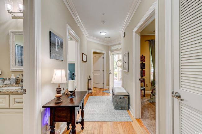 Corridor with crown molding, a sink, light wood-style floors, baseboards, and visible vents | Image 4