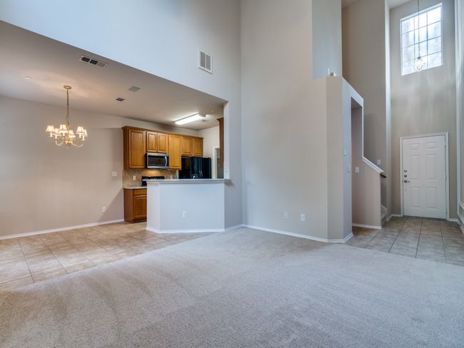 Unfurnished living room with a high ceiling, a chandelier, light carpet, and light tile patterned flooring | Image 6