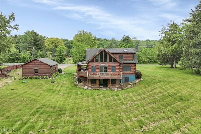 Back of house featuring log siding, a deck, a lawn, and a view of trees | Image 47