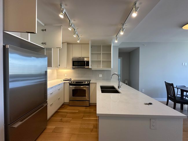 Kitchen featuring stainless steel appliances, a sink, a peninsula, light wood finished floors, and open shelves | Image 20