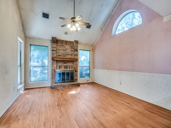 Unfurnished living room featuring wood finished floors, a ceiling fan, a fireplace, a textured ceiling, and high vaulted ceiling | Image 5