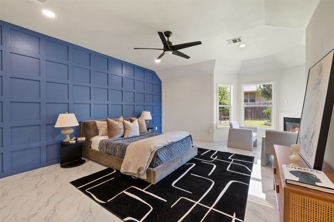 Bedroom with light marble finish floors, a decorative wall, a glass covered fireplace, ceiling fan, and vaulted ceiling | Image 19