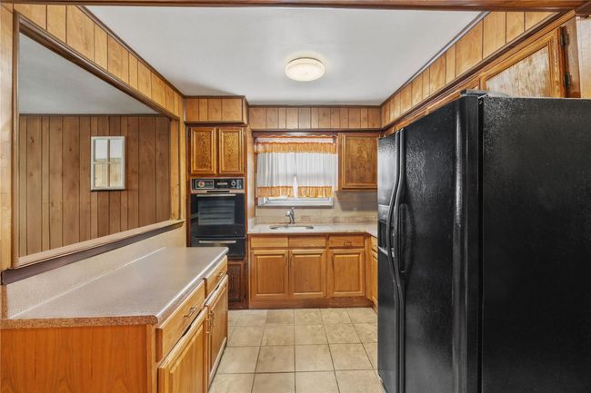 Kitchen featuring black appliances, wooden walls, light countertops, brown cabinetry, and a warming drawer | Image 15