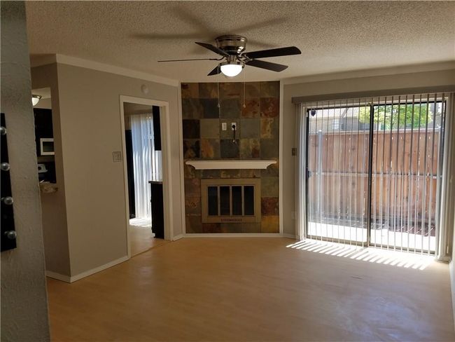 Unfurnished living room featuring ceiling fan, wood finished floors, a textured ceiling, a fireplace, and crown molding | Image 4