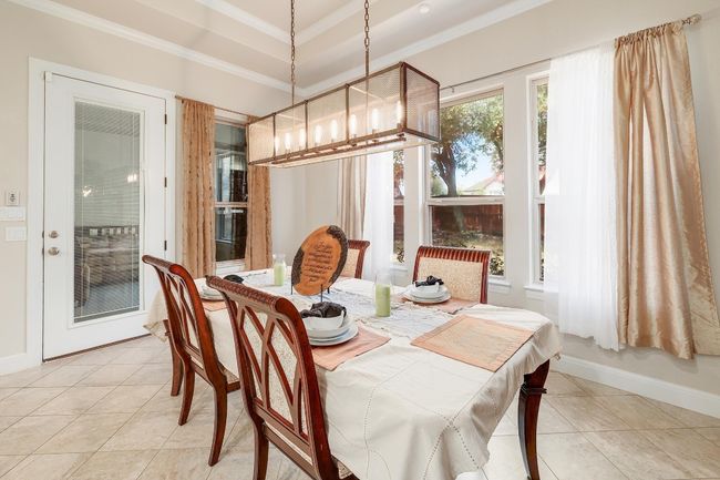 Dining space with light tile patterned floors, a chandelier, ornamental molding, and a tray ceiling | Image 6