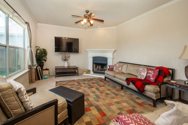 Living room with a ceiling fan, ornamental molding, a fireplace with raised hearth, and carpet floors | Image 8