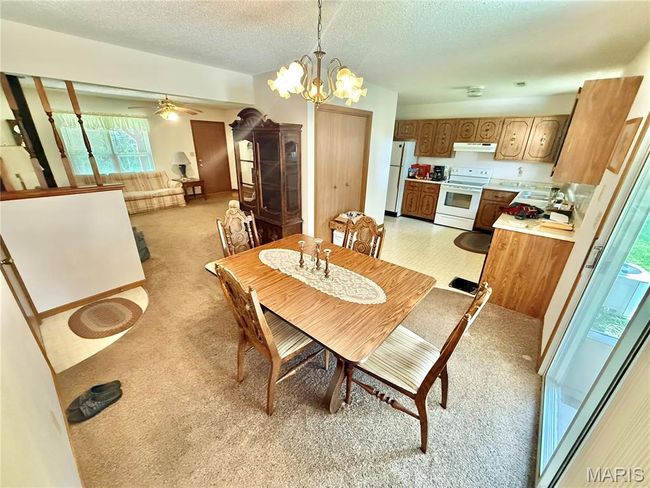 Dining room with a textured ceiling, light carpet, a chandelier, and ceiling fan | Image 23
