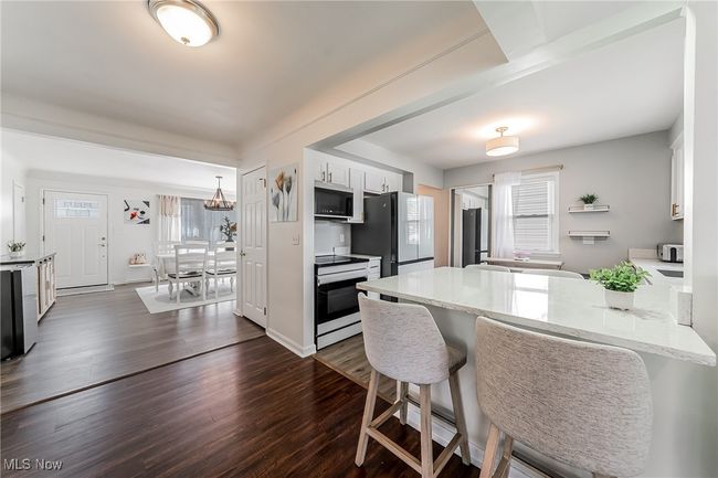 Kitchen with a kitchen bar, a peninsula, white appliances, white cabinets, and dark wood-type flooring | Image 16