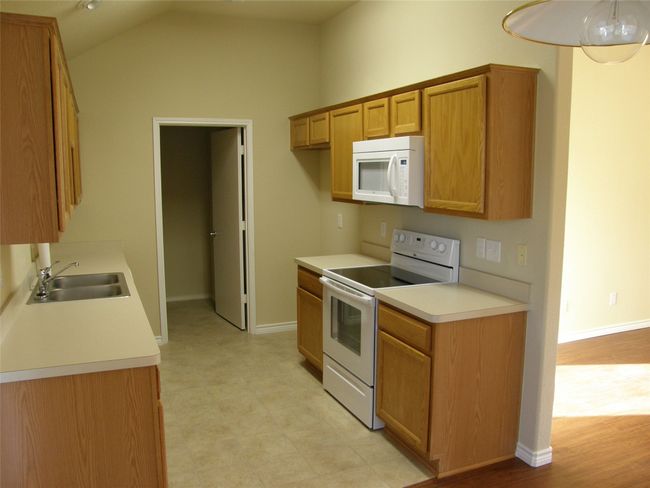 Kitchen featuring white appliances, light countertops, lofted ceiling, brown cabinetry, and light floors | Image 6