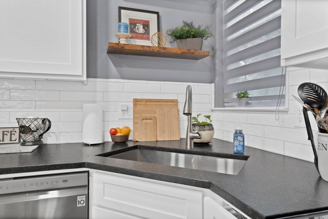 Kitchen with stainless steel dishwasher, a sink, white cabinets, backsplash, and dark countertops | Image 23