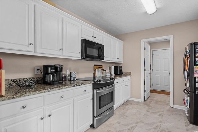 Kitchen featuring electric range, black microwave, white cabinets, stone countertops, and a textured ceiling | Image 7