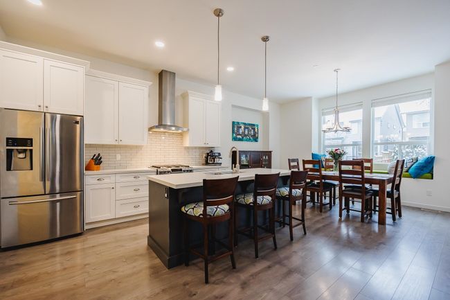 Kitchen with light countertops, wall chimney range hood, a center island with sink, stainless steel fridge, and tasteful backsplash | Image 7