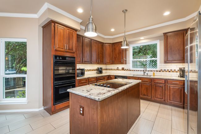 Kitchen featuring black appliances, tasteful backsplash, light stone counters, crown molding, and decorative light fixtures | Image 18