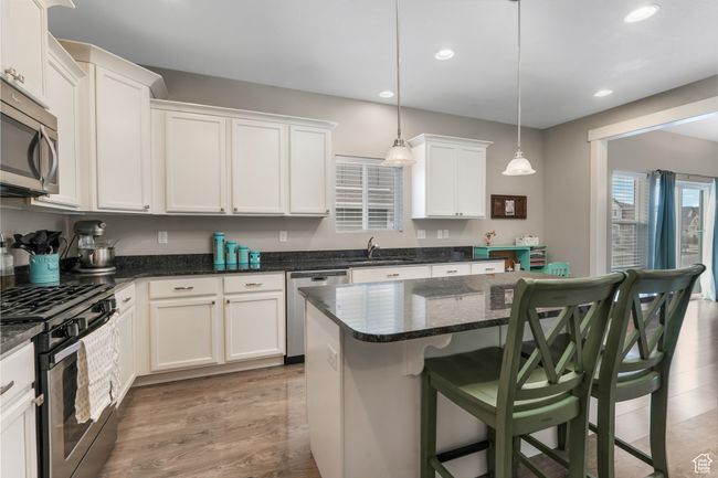 Kitchen with white cabinets, stainless steel appliances, recessed lighting, light wood-style floors, and a kitchen breakfast bar | Image 9
