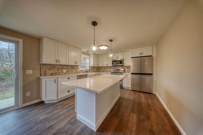 Kitchen featuring a sink, white cabinets, decorative backsplash, dark wood finished floors, and appliances with stainless steel finishes | Image 8