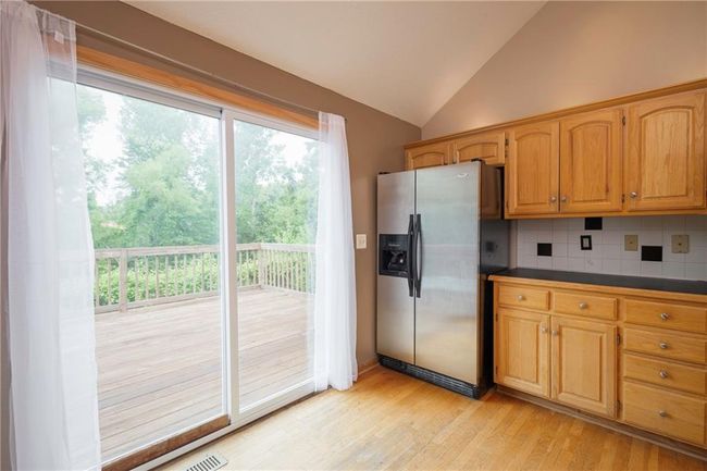 Kitchen with stainless steel fridge, lofted ceiling, light wood finished floors, backsplash, and dark countertops | Image 14