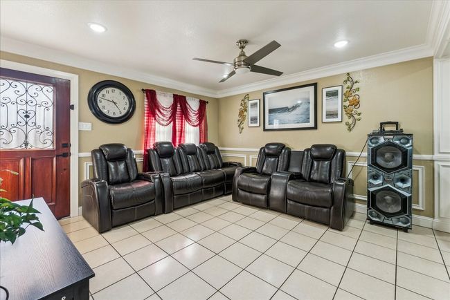 Home theater room with light tile patterned floors, a wainscoted wall, ornamental molding, and ceiling fan | Image 18