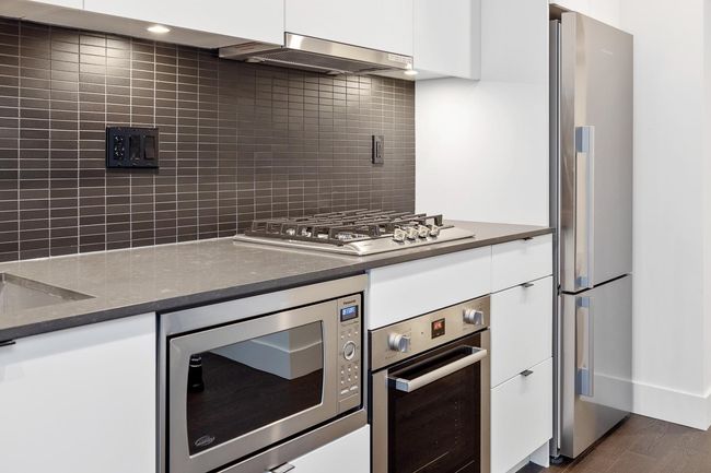 Kitchen featuring stainless steel appliances, wall chimney range hood, white cabinetry, and backsplash | Image 25