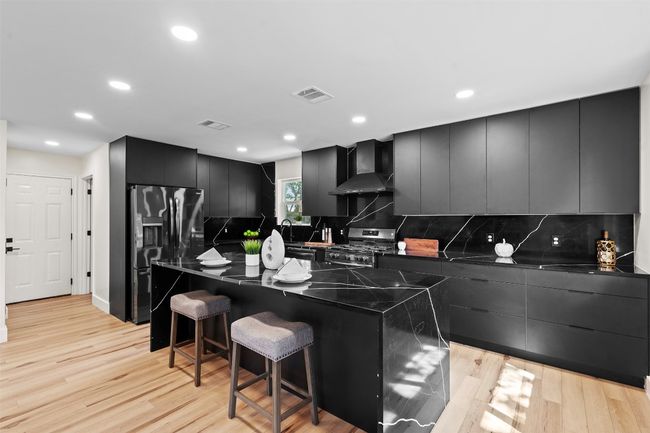 Kitchen with wall chimney exhaust hood, black fridge, stainless steel range with gas stovetop, modern cabinets, and dark countertops | Image 7