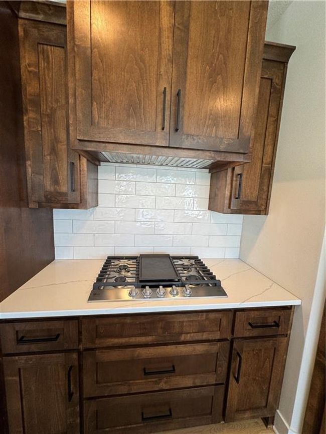 Kitchen featuring stovetop, tasteful backsplash, dark brown cabinets, and light stone counters | Image 23