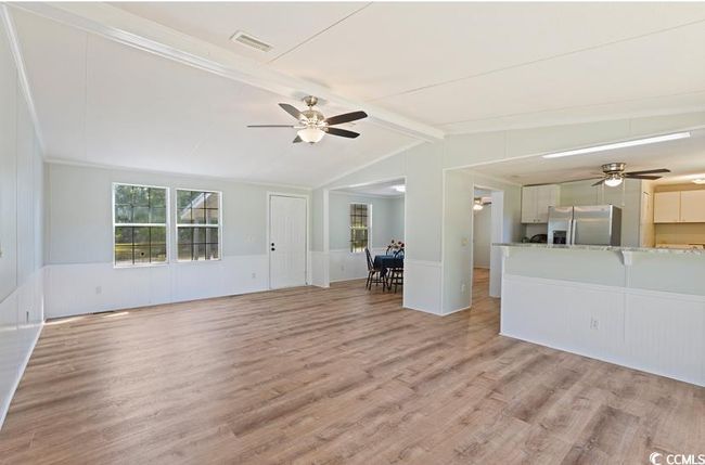 Unfurnished living room featuring a ceiling fan, light wood finished floors, a wainscoted wall, and a decorative wall | Image 10